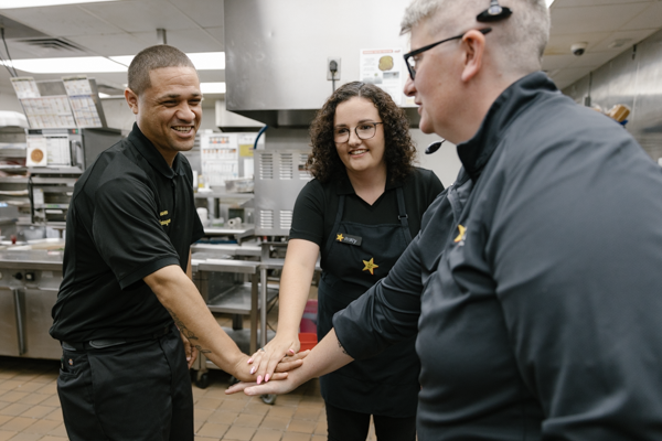 Three Hardee's employees stand with their hands in a circle