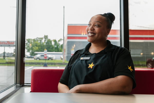 Ashley is a Hardee's employee who is smiling and sitting at a booth